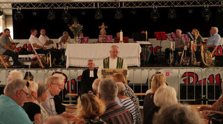 Pfarrer Erwin Bertsch (Mitte) predigt im Festzelt. Im Hintergrund zu sehen sind Pfarrer Christian Noeske und auf der Bühne der Ketscher Posaunenchor.