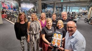 Gerhard Waldecker vertritt die Gemeinde Plankstadt beim Pre-Opening und überreicht Geschäftsführerin Vanessa Steiger-Dehner Tassen der Gemeinde für die Mitarbeitenden im Cube Story Plankstadt by Fahrrad XXL. Gerald, Christiane und Céline Moll (v. l.) als Bauherren gratulieren Sven Dehner sowie Renate und Martin Steiger von der Firma Fahrrad XXL Kalker GmbH.