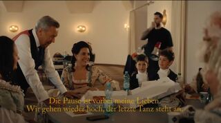 Aus dem Video „Gut, dass ihr da seid“ eine Szene, bei der Roland Kaiser am Tisch beim Pizzaessen steht und sich mit den Tänzern unterhält.