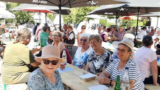 Aufmerksame Zuhörer unterm Sonnenschirm: Die hochsommerlichen Temperaturen sorgen zum einen für Durst beim Publikum, zum anderen dafür, dass die schattigen Plätze auf dem Messplatz besonders begehrt sind.