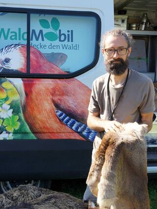 Dr. Marco Ieronimo von der Schutzgemeinschaft Deutscher Wald zeigt vor dem Waldmobil eine Rehdecke.