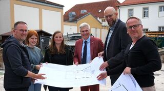 Ein Blick in die Pläne von Architekt Christopher Ansorge (r.): Pfarrer und Dekan Uwe Lüttinger (v. l.), Kindergarten-leiterin Lena Loesche, Janina Sessler von der Geschäftsführung Kindertageseinrichtungen, Erster Bürgermeister Matthias Steffan und Amtsleiter Roland Strieker stehen auf der Bodenplatte des Neubaus.