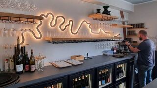 Die Vinothek im Weingut Sermann im Oktober 2023 ist ein moderner „Place to be“. Die Ahr fließt ruhig hinterm Haus und als schwungvolle Beleuchtung im Innenraum.