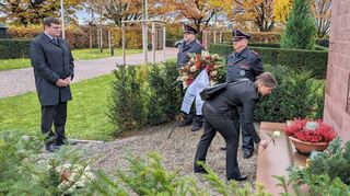 Im Beisein von Bürgermeister Nils Drescher (links) und der Ehrenwache der Freiwilligen Feuerwehr legt Pfarrerin Christiane Banse eine weiße Rose nieder.