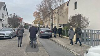 Weil die Autos rechts und links in der Ehehaltstraße auf dem Bordstein parken, muss Waltraud Wettstein mit dem Rollstuhl auf der Straße fahren. Den Rollstuhl schiebt Götz Junk, daneben läuft Sigrid Schüller.
