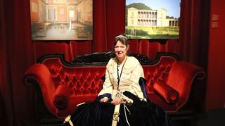 Die Museumspädagogin Petra Henke als Königin Therese auf dem roten Samtsofa vor den Bildern der Villa Ludwigshöhe.