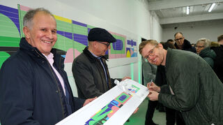 Florian Budke signiert ein Bild der Kunst-Wand, das Bauherr Andreas Epple (l.) an Oberbürgermeister Dr. René Pöltl überreicht hat. Bild: Widdrat