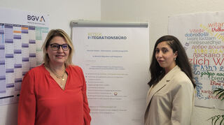Flüchtlings- und Integrationsbeauftragte Nicole Verclas (l.) und Latifa Yasemine Yahia Cherif vom DRK vor einem zusammenfassenden Plakat ihrer Arbeit.