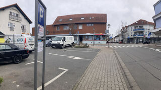 Der Parkplatz (l.) könnte für Stellplätze der Gebäude rund um die Kreuzung vorgeschrieben sein, in dem mehrere Geschäfte und Wohnungen zu finden sind. Sie gehören auch der gleichen Eigentümerfamilie.