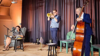 Das Künstlertrio bringt gemeinsam das Paris der 1920er-Jahre in den Gemeindesaal: Autorin Britta Habekost (v. l.), Trompeter Thomas Sifflung und Kontrabassist Thomas Debus erschaffen gemeinsam eine sehr dichte Atmosphäre.