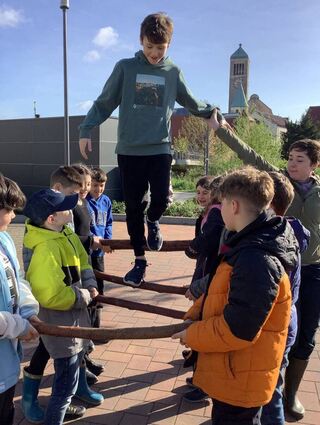 Gemeinsam bilden die Schüler mit dicken Holzstöcken eine Hängebrücke, über die sogar balanciert werden kann.