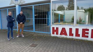 Klimaschutzmanagerin Julia Berberig und Bauamtsleiter Marc Schneider vor dem Eingang zum Schwimmbad: Direkt vor ihnen auf dem Boden zeigen zwei kleine Schachtdeckel an, dass dort die Fernwärmeleitung der MVV verläuft.