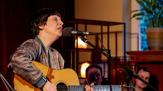 Jeanette Hubert tritt mit der Gitarre ans Mikrofon bei der Veranstaltungsreihe und Liedermacher-Show „Ulis Wohnzimmer“ mit Ulrich Zehfuß, zu der er Gäste aus der deutschen Liedermacher-Szene einlädt.