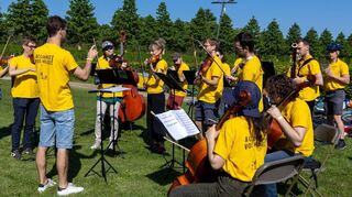 Erste Station der Konzertreise per Fahrrad: Raphael Merlin (3. v. l.) dirigiert sein Orchester „Les Forces Majeures“ im Schlossgarten auf der Blumenwiese. Auf den Shirts tragen die Musiker die Aufforderung: „Accordez vos vélos“ (Stimmen Sie Ihre Fahrräder).