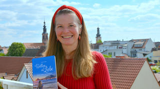 Sandra Andrés mit ihrem Roman „Wellen der Liebe“ mit ihrem Ausblick auf Schwetzingen im Hintergrund.