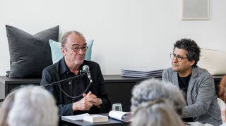 Auf einer vom Verein zur Förderung des Kulturdialogs organisierten Lesung befindet sich der Autor Robert Menasse im Gespräch mit Mustafa Al-Slaiman. Die Lesung wird vom Musiker Bernhard Sperrfechter an der Gitarre mit Improvisationen umrahmt.