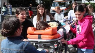 Die Schülerinnen rollen die Fahrtrage des Deutschen Roten Kreuzes über das Schulgelände des Gymnasiums – Leonie spielt für den Übungsfall die zu rettende Patientin.