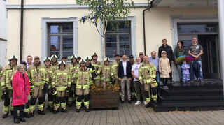 Symbol des Willkommens für den neuen Bürgermeister: Kevin Weirether (11. v. r., dunkles Jackett) freut sich über die Birke, die die Freiwillige Feuerwehr und der Bauhof für ihn gestellt haben. Von seinem Dienstzimmer hinterm Balkon hat er sie stets im Blick.