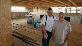 Bürgermeister Nils Drescher (l.) und Haustechnikplaner Dietmar Defièbre auf den Rängen der neuen großen Sporthalle, die imposant von Holzdecken überspannt wird.