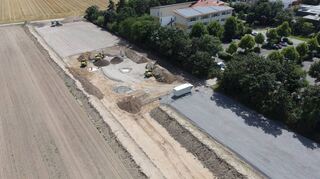 Sehr gut zu erkennen, ist der Fortschritt auf der Baustelle aus der Vogelperspektive. In der Bildmitte ist die Markusschule zu erken-nen, rechts davon der katholische Kindergarten und die Rheinfrankenhalle. Die graue Fläche rechts zum Bewuchs hin wird zum Parkplatz, der Bereich bis zum Acker als Bienen- und Blühwiese ausgewiesen. Am linken Ende der Fläche entstehen Soccercourt und Multifunktionsspielfeld, dazwischen die Pumptrackanlage. Zum Grünstreifen hin wird ein Fuß- und Radweg angelegt.