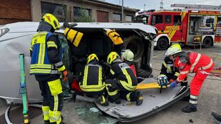 Übungsszenario: Ein Auto liegt nach einem Unfall auf der Seite, eine Person befindet sich eingeklemmt im Wagen. Gemeinsam retten Feuerwehr und Johanniter.