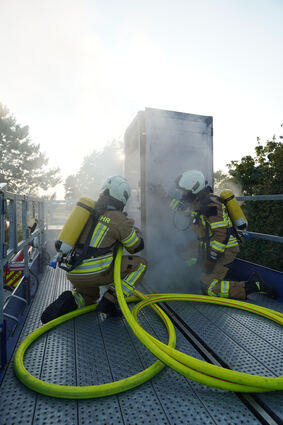 In den blauen Container gibt es für die Feuerwehr zwei Einstiegsmöglichkeiten, um an den Brandherd am Inneren heranzukommen: Über eine Tür und, wie hier zu sehen ist, über das Dach.