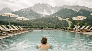 Im klimapositiven Hotel Leitlhof schwimmen die Gäste im großem beheizten Außenpool mit Blick auf die atemberaubende Bergkulisse.