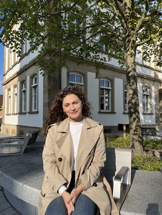 Linda Hoti sitzt an der Friedenslinde in der Ortsmitte der Gemeinde. Für sie ist es ein Ort der Begegnung, die ihr ohnehin sehr wichtig ist.