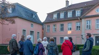 Heide Roth-Bühler alias Cordula de Pigage ist hier vor dem Amtsgericht zu sehen. Das Gebäude wurde 1725 als Prinzenhaus erbaut. Ab 1753 diente es als Gesandtenhaus. Dort wohnten Nicolas de Pigage, Friedrich Ludwig Sckell, Johann Michael Zeyher, Friedrich Wilhelm von Brand und Andreas von Riaucour. Der Dichter Johann Peter Hebel verstarb hier 1826.