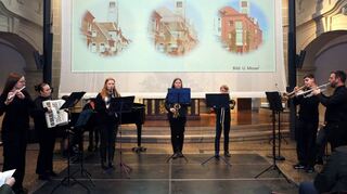 Das Bläser-Ensemble des Gauß-Gymnasiums unter der Leitung von Bernhard Sommer umrahmt die Gedenkfeier, im Hintergrund sind Bilder jüdischen Lebens in der Stadt zu sehen.