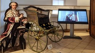 In der Ausstellung „CabineT“ im Karl-Wörn-Haus ist dieser nachgebaute Gartenphaeton von Carl Theodor zu sehen. Auf dem Bild-schirm läuft gerade ein Film, in dem unser Autor dieser Kurzserie Dr. Ralf Wagner den Kurfürsten Carl Theodor spielt.