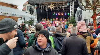 Zahlreiche Menschen besuchen den Weihnachtsmarkt, im Hintergrund hat die Markusschule ihren Auftritt auf der Bühne.