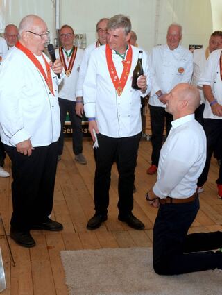 „Kochen im Grünen“: Kniend erhält Bürgermeister Timo Wangler die Auszeichnung „Löffeltrunk“ der Chuchis.