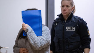 Die wegen Mordes durch Unterlassung angeklagte Frau (l.) wird zum Auftakt des Prozesses im Landgericht Heidelberg von einer Justizbeamtin in den Gerichtssaal geführt.