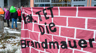 Ein Transparent mit der Aufschrift „Haltet die Brandmauer“ hängt auf einer Kundgebung.