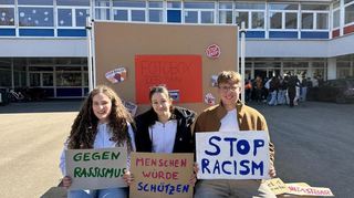 Die Schülerinnen Chiara Schmitt, Jasmine Schubardt und Schüler Moritz Neumann halten Schilder mit Botschaften in der Fotobox der SMV in die Höhe.