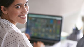Working with a smile. A young woman happily working at her computer
