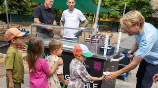 Markus Krampe, Mitveranstalter des Glücksgefühl Festivals, gibt kostenloses Eis an die Kinder des Friedrich-Fröbel Kindergarten aus. Hinten beobachten Oberbürgermeister Marcus Zeitler und der Inhaber der Eisdiele "holy ice" Michael Heiliger das Geschehen.