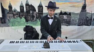 Julian Seiler begleitet die Vernissage am Keyboard vorm Bild einer beeindruckenden Stadtsilhouette.