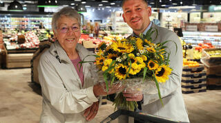 Marktleiter Sven Lempke begrüßt Irene Lamatsch aus Mannheim-Rheinau als erste Kundin des neuen Brühler Scheck-in-Marktes mit einem Blumenstrauß.