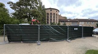 Hinter dem Bauzaun ist der Arm einer Baumaschine zu erkennen. Das zeigt: Es tut sich was.