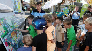 Auf dem Wimmelbild müssen die Kinder Verkehrssituationen erkennen und beschreiben. Anna Krebs (hinten l.) und Tanja Pietrus Biebel (2. v.r., Verkehrsprävention Heidelberg) erläutern die Situationen.