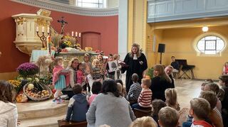 Pfarrerin Isabelle Schwiderski mit Kindern, die alle guten Gaben mit Bildern zeigen, vor dem mit Lebensmitteln dekorierten Altar.
