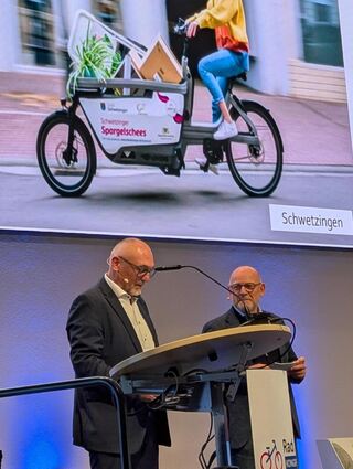 Der AGFK-Vorsitzende Günter Riemer (l.) und Verkehrsminister Winfried Hermann vor einem Bild der Schwetzinger "Spargelschees".