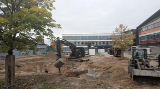 Ein Bagger füllt auf dem Pausenhof des Hebel-Gymnasiums Erde in die ausgehobene Baugrube für die Versickerungsrigole.