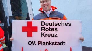 Lukas Damm mit dem Schild vom DRK Plankstadt, das am medizinischen Zentrum im Carl-Benz-Stadion angebracht wird.