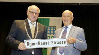 <p>Roland Seidel überreicht Helmut Baust das Straßenschild mit dessen Namen.</p>